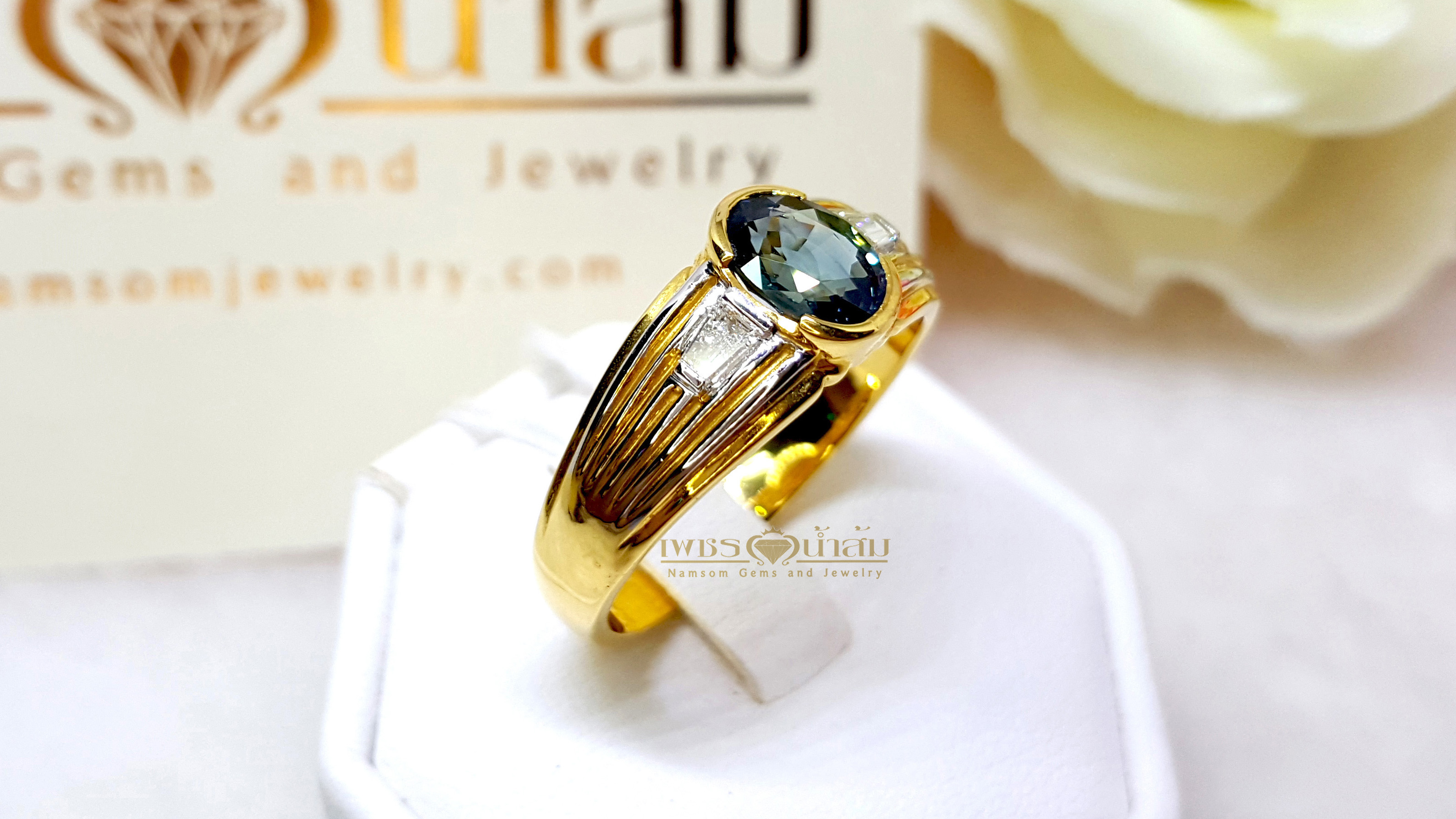 แหวนพลอยไพลิน Blue Sapphire สีอมเขียว ประดับตกแต่งด้วยเพชรแท้เจียรเหลี่ยมแบเก็ต และบากลายทางที่ขอบข้าง